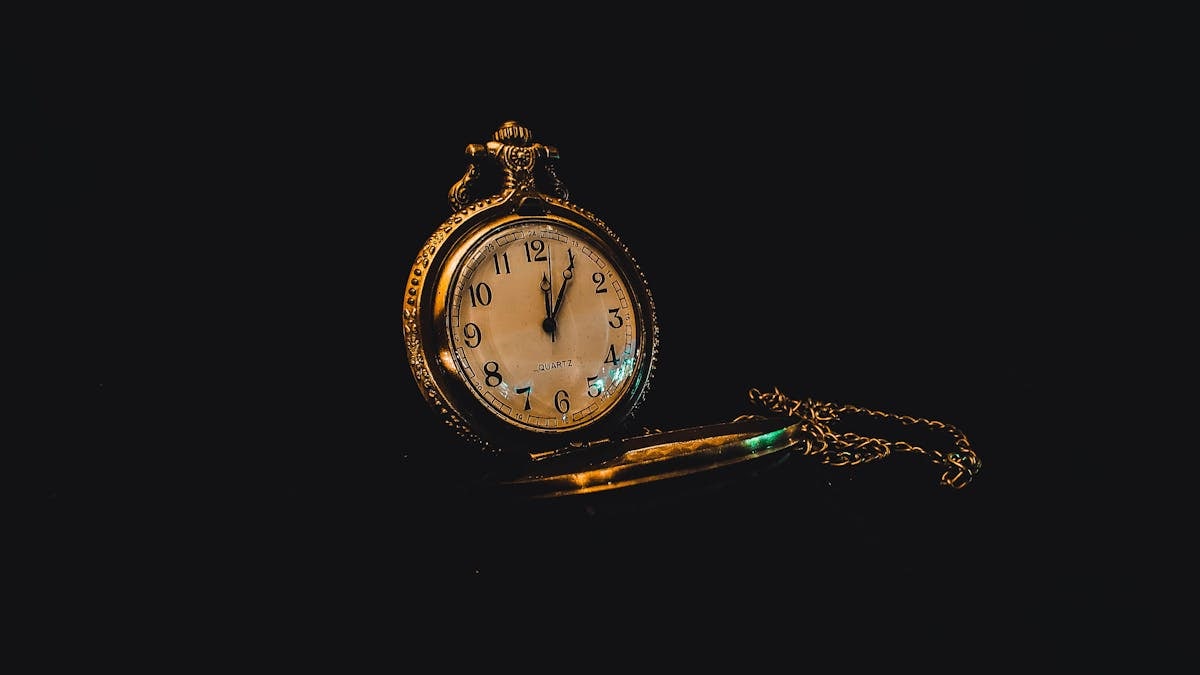 Golden decorative shiny retro watch with chain placed on dark black surface in studio
